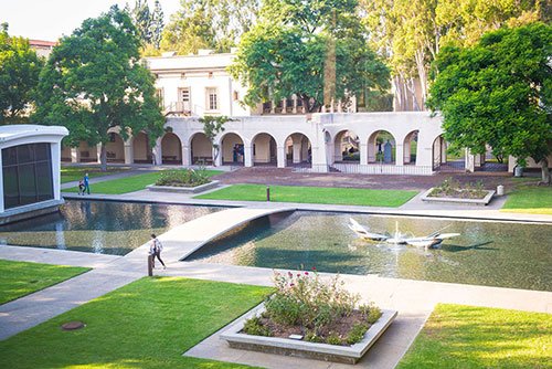 Image of the beautiful Caltech Campus showing building with arches, a pond and a bridge over it